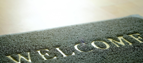 Welcome mat with gold writing on wooden floor
