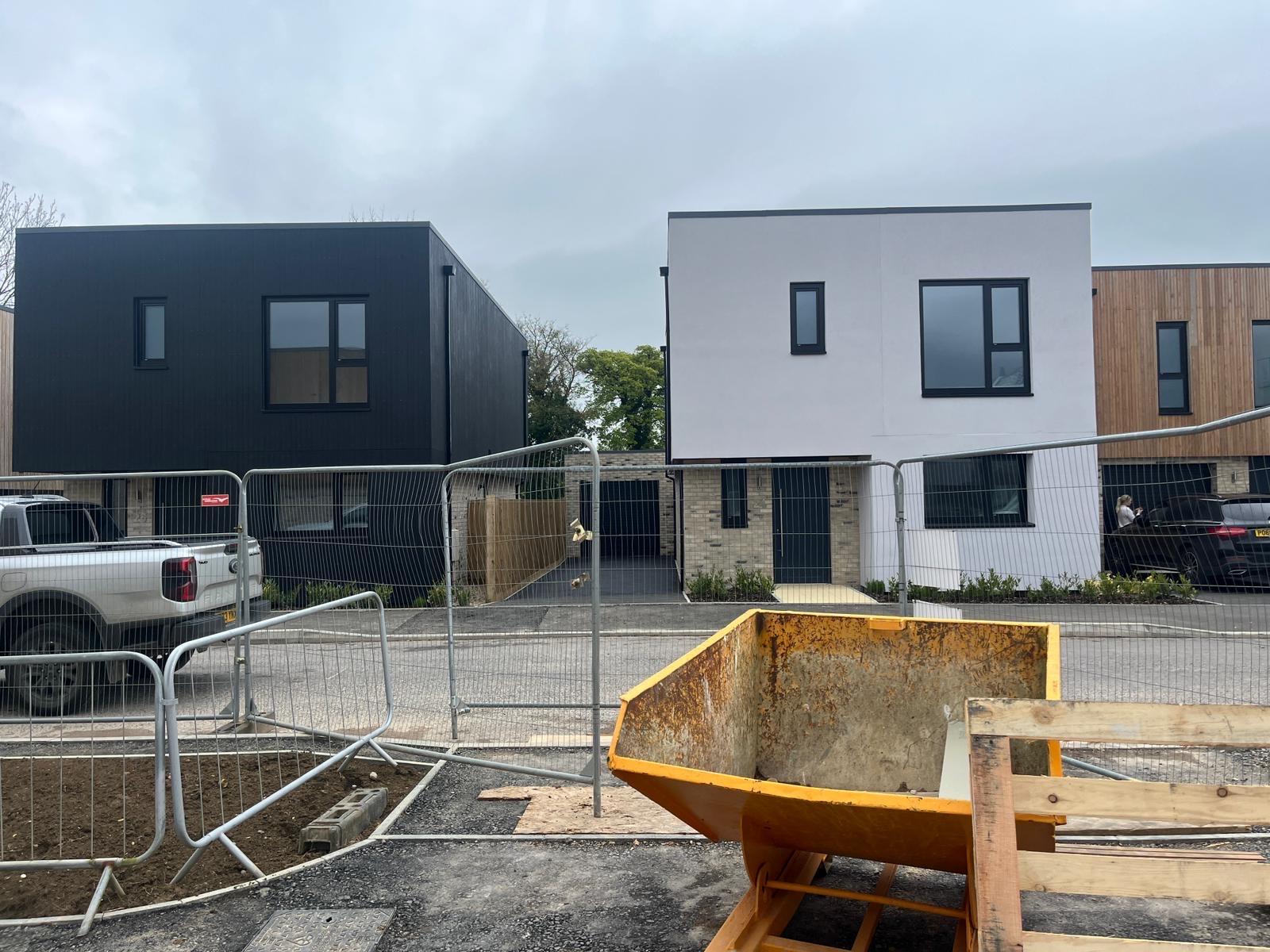 Two modern buildings, white and black with safety fencing in front and a skip.